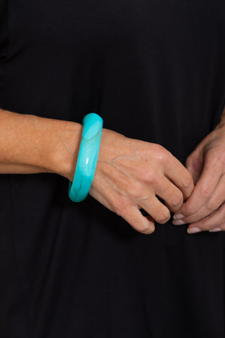 Narrow Resin Bangle in Aqua, close up on model wrist against a black background.