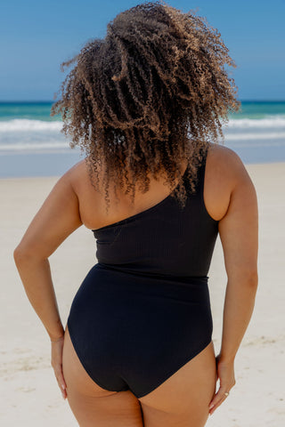Esperance Core Support One Piece Swim in Black Texture, back view on model at the beach.