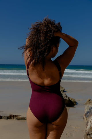 Sorrento Core Support One Piece Swim in Dark Cherry Texture, back view on model at the beach