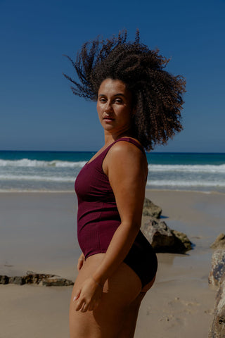 Sorrento Core Support One Piece Swim in Dark Cherry Texture, side view on model at the beach