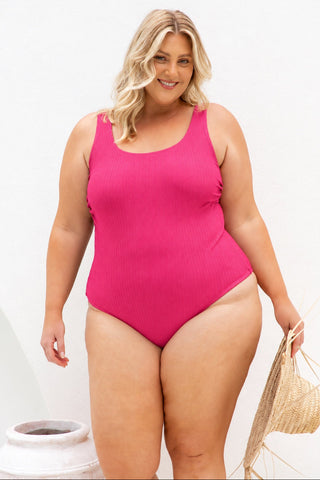 Sorrento Core Support One Piece Swim in Raspberry Texture, front view on model holding a woven bag against a white wall.
